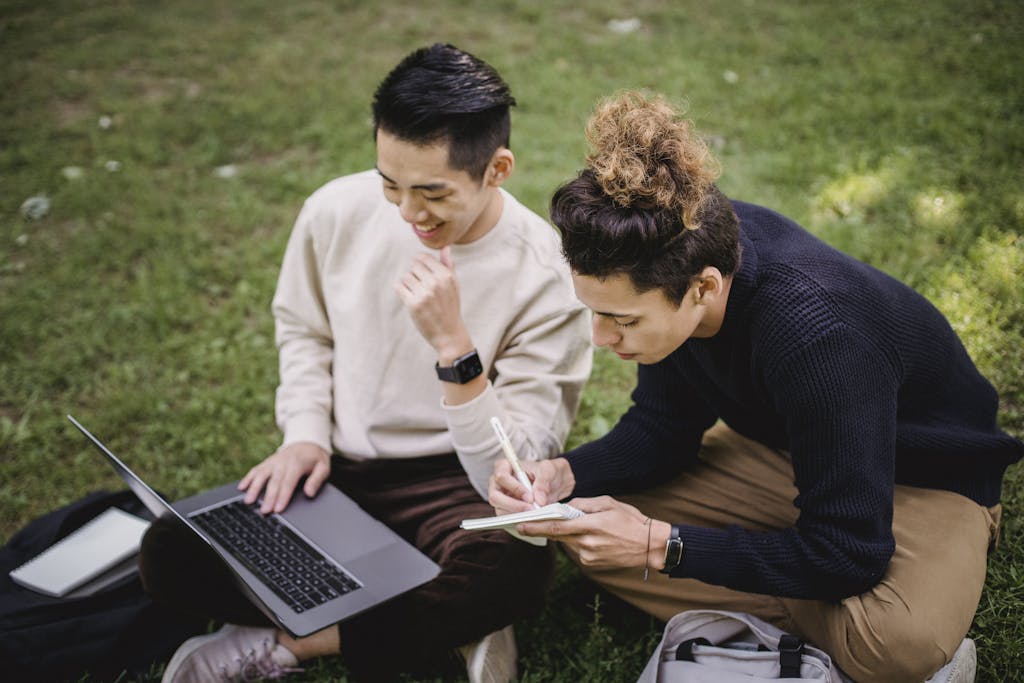 Two young men studying together on a laptop in an outdoor park setting.